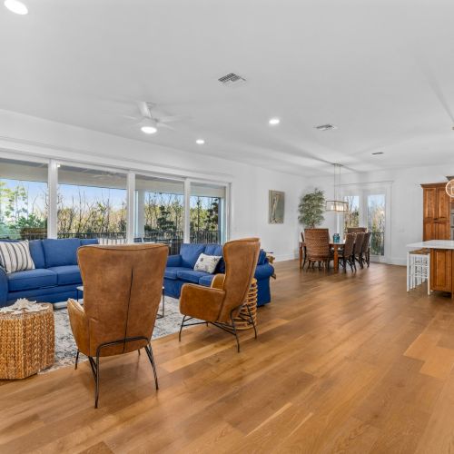 Open room with wood floor, blue sofa, two brown chairs, dining table, and kitchen island