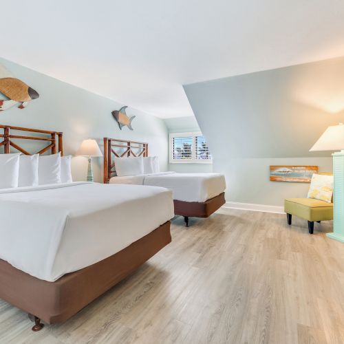 Spacious bedroom with two queen beds, coastal artwork, and light wood flooring