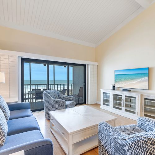 Living room with blue couch, armchairs, TV, and balcony view.
