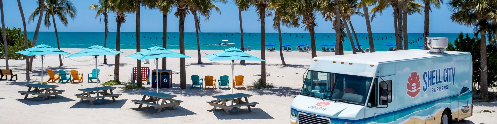 Shell Way food truck parked on a tropical beach with picnic tables and palm trees