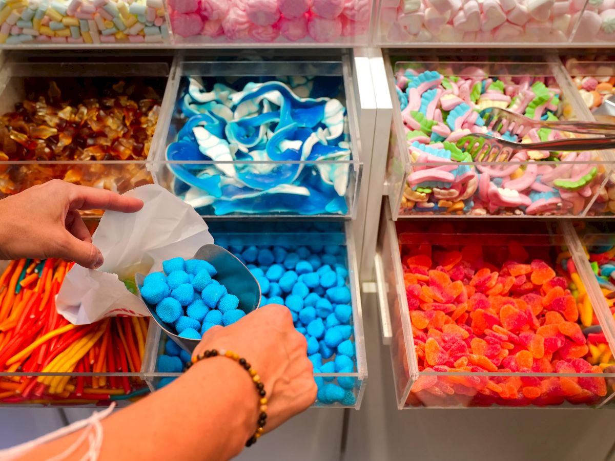 candy store. Woman hand with scoop taking colorful delicious candies on counter of shop, grocery, market, cafe. Many colorful candies on grocery stand Dessert, sale, sweet food and confectionery concept.
