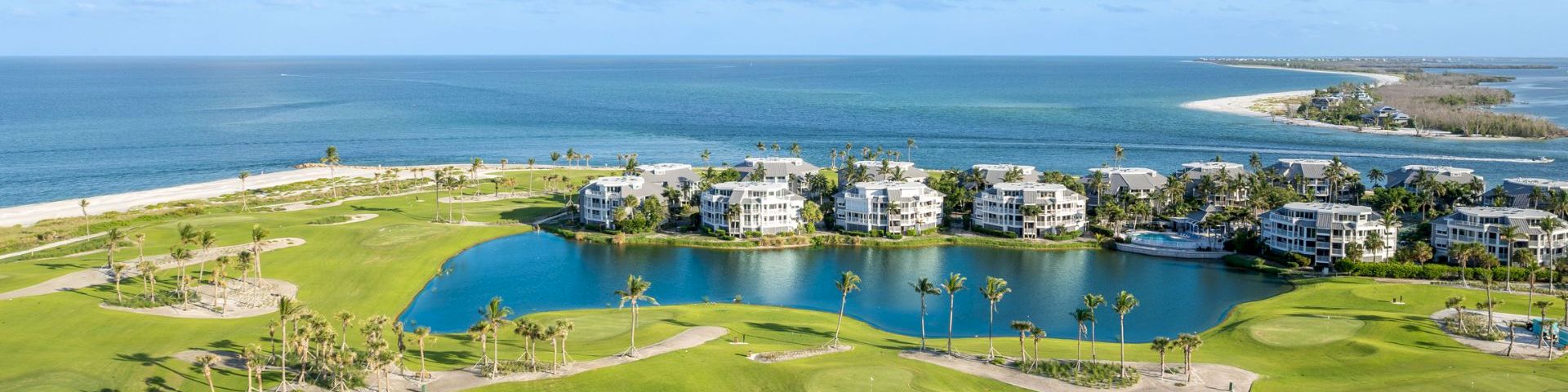 Aerial view of coastal condos and golf greens by the water.