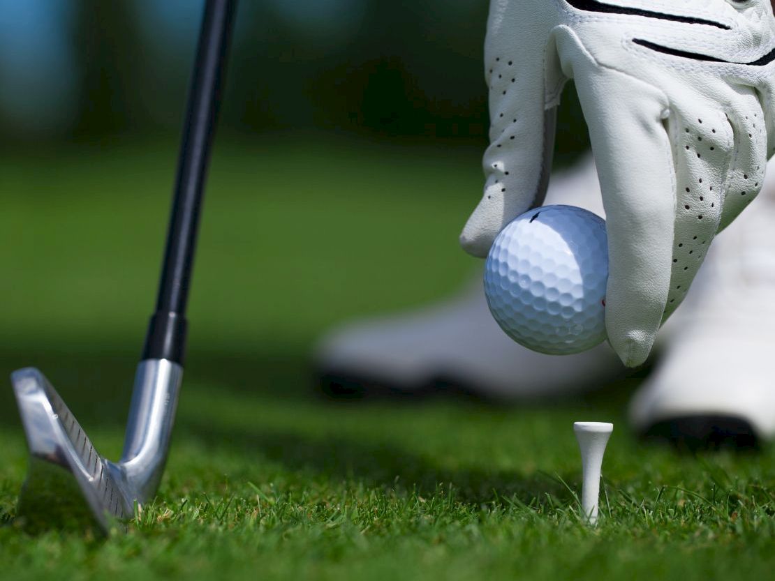 Golfer placing ball on tee with club ready