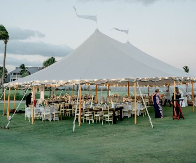 A large white event tent with warm string lights set on a green lawn, styled for a wedding reception.
