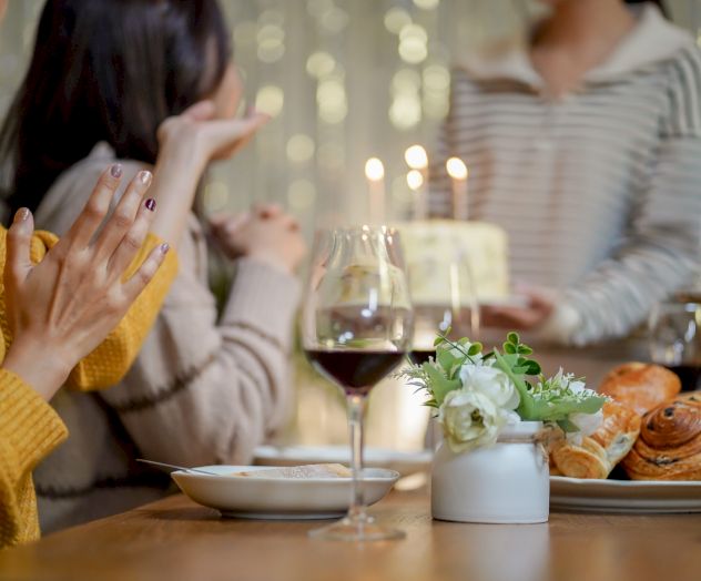 Two people dining at a candlelit table, clinking/holding wine glasses and sharing a meal.
