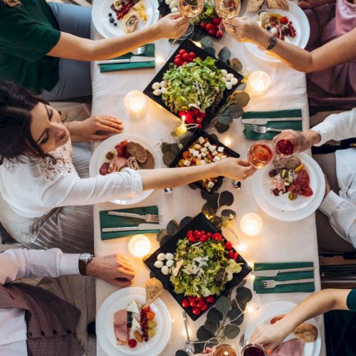 A top view of big family sitting at a table on a indoor birthday party, clinking glasses. A midsection.