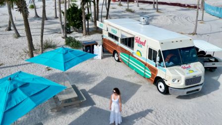 Aerial view of Island Tacos food truck on the beach with umbrellas and palm trees