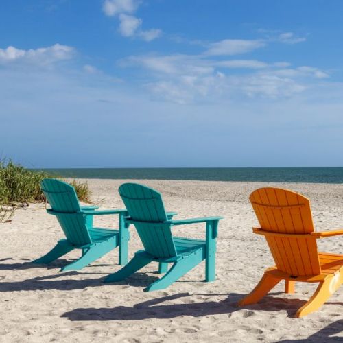 Three wooden beach chairs on sand facing the ocean