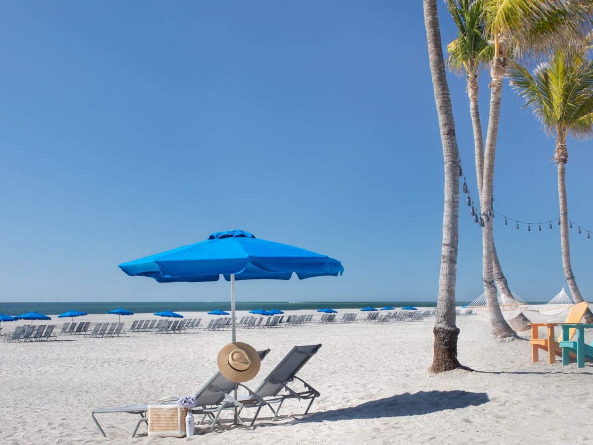 Two beach chairs under a blue umbrella on a sunny day