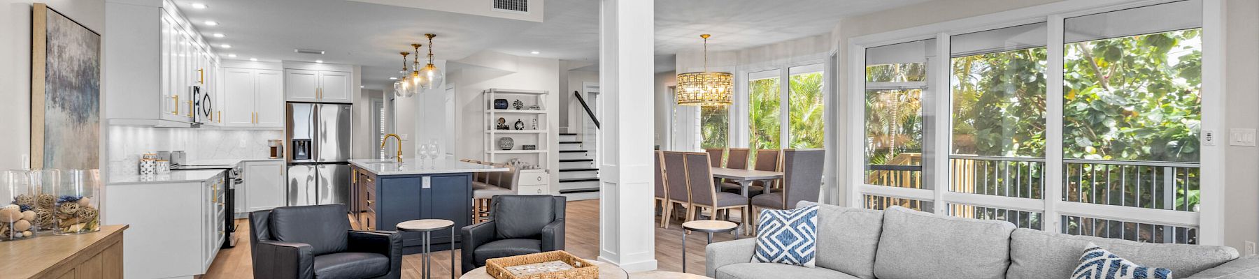 Gray sectional, two round tables, large windows, open kitchen and dining.