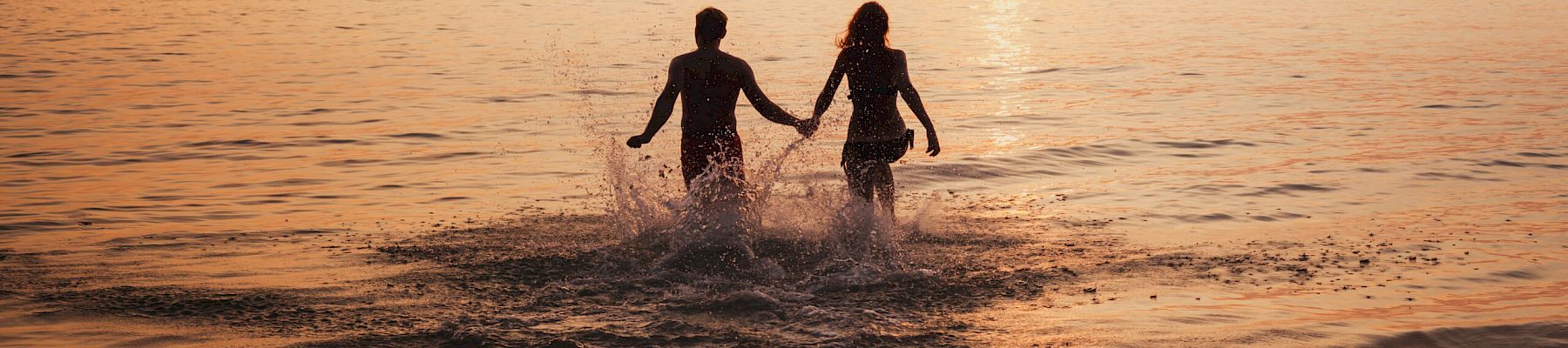 silhouette of couple on sea beach at sunset, happy holidays for two, man and woman holding hands and running to water