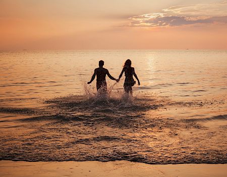 silhouette of couple on sea beach at sunset, happy holidays for two, man and woman holding hands and running to water