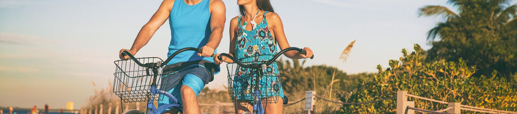 Beach couple biking enjoying leisure sport recreational activity relaxing outdoors at sunset. Young woman and man riding bicycles on USA Florida vacation. Summer people lifestyle happy.