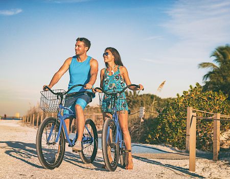 Beach couple biking enjoying leisure sport recreational activity relaxing outdoors at sunset. Young woman and man riding bicycles on USA Florida vacation. Summer people lifestyle happy.