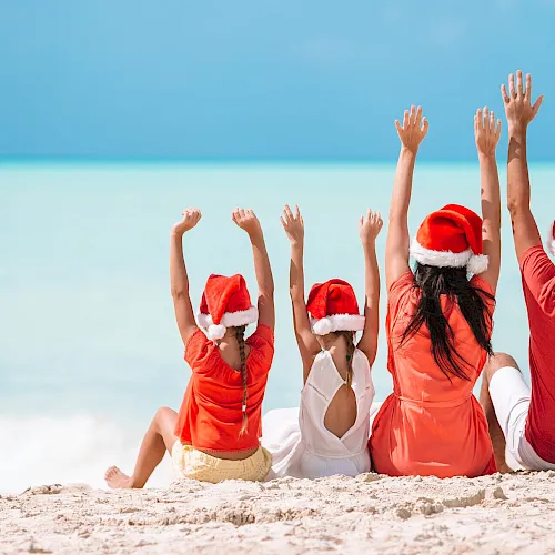 Happy family in Santa hats on a tropical beach celebrating Christmas vacation
