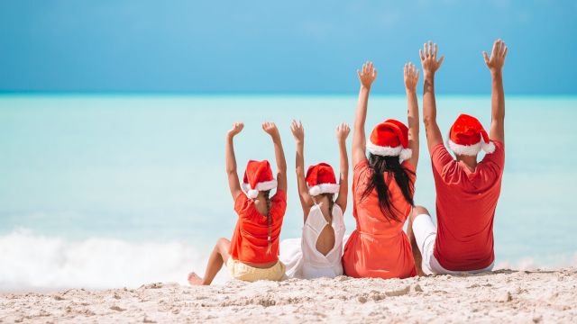 Happy family in Santa hats on a tropical beach celebrating Christmas vacation