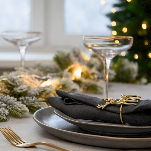 Christmas table setting with elegant empty gray plates decorated gold napkin ring near Xmas tree. Family holiday dinner at home. Close up.