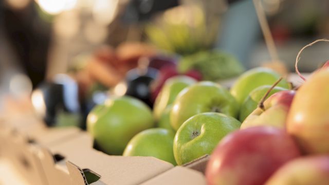 Natural organic food and health. Close up of fresh ripe green apples at farmers market, selective focus. Cardboard boxes full of various local seasonal fruits and vegetables on greenmarket stall
