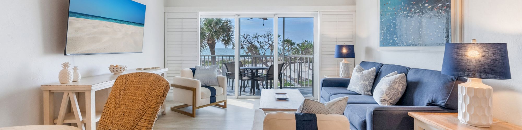 Couch and chairs in living room, TV on wall, view of balcony with palm trees