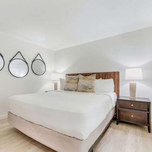 Bed with two pillows, two lamps on nightstands, and three round mirrors on the wall