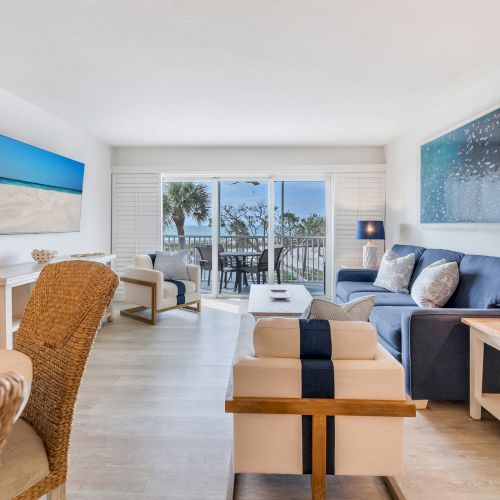 Couch and chairs in living room, TV on wall, view of balcony with palm trees