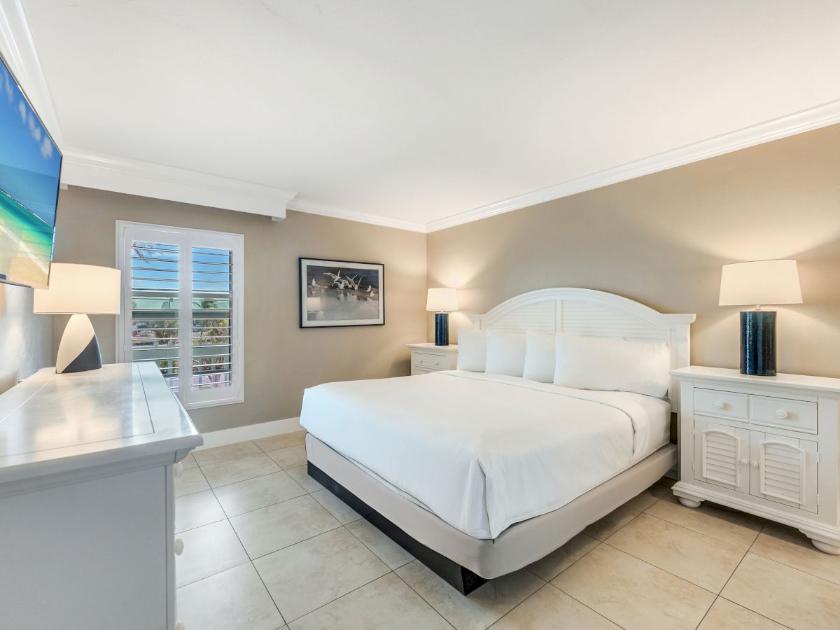 Bedroom with a white bed, two nightstands and a wall mounted TV.
