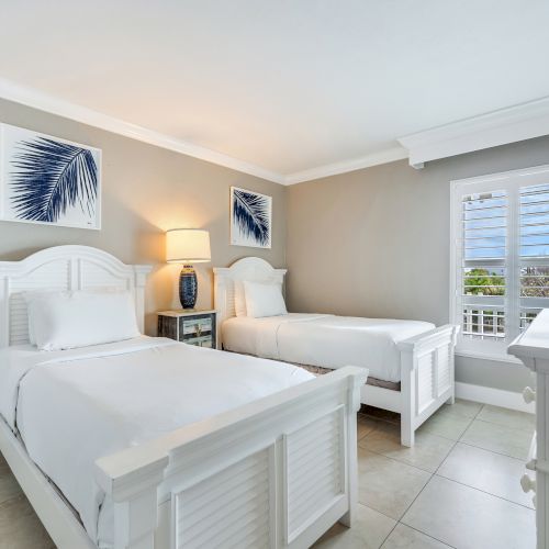 Bedroom with two white twin beds, nightstand, and window.