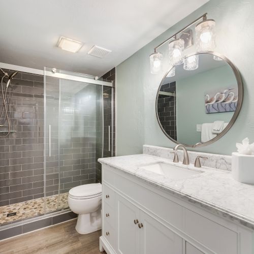 Elegant bathroom with a walk-in shower, dark tile wall, and a round mirror above a white vanity