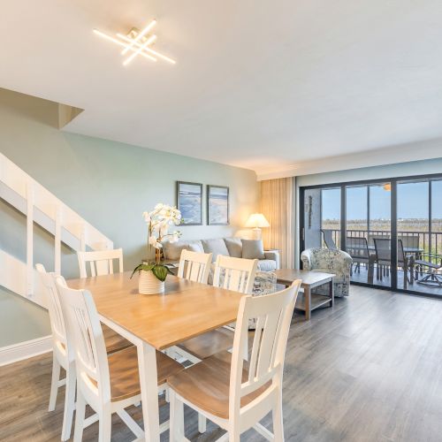 Dining space with a wooden table and white chairs next to a staircase and pastel green walls