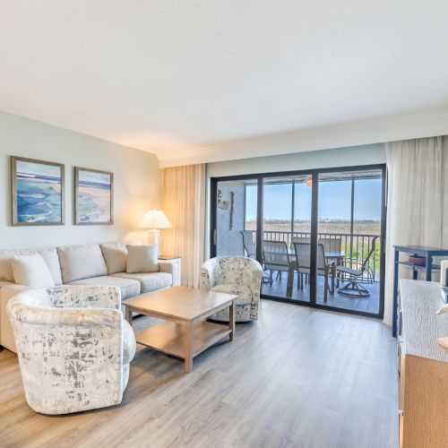 Living room with plush seating, wood floors, and a balcony view of the ocean.