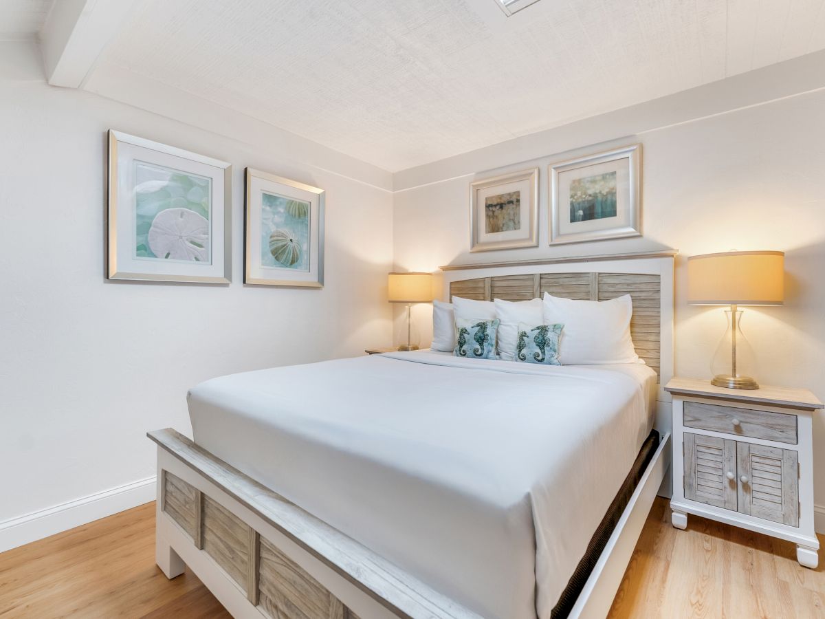 Bed with white bedding, two nightstands with lamps, and framed pictures on the wall.