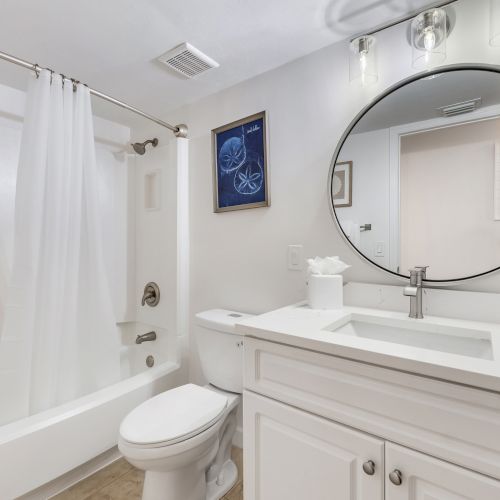 Bathroom with tub, toilet, and round mirror.