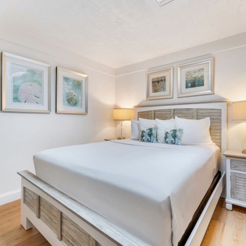 Bed with white bedding, two nightstands with lamps, and framed pictures on the wall.