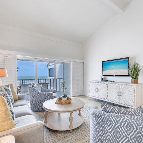 Sofa, chairs, coffee table, TV, and balcony view.
