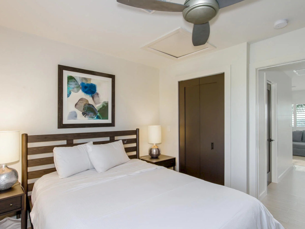Bedroom with white bedding, dark wood bed frame, and a ceiling fan