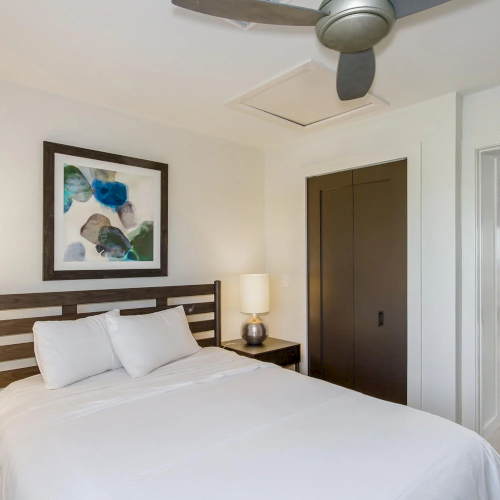 Bedroom with white bedding, dark wood bed frame, and a ceiling fan