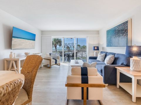Couch and chairs in living room, TV on wall, view of balcony with palm trees