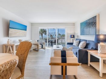 Couch and chairs in living room, TV on wall, view of balcony with palm trees
