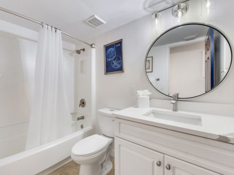 Bathroom with tub, toilet, and round mirror.