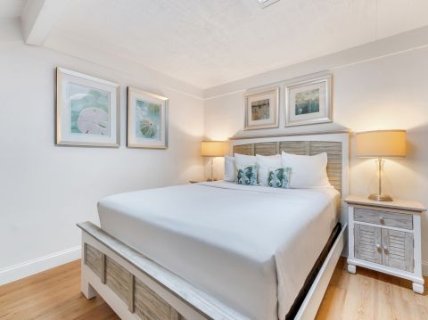 Bed with white bedding, two nightstands with lamps, and framed pictures on the wall.