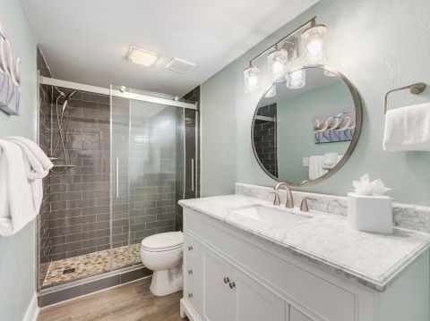 Elegant bathroom with a walk-in shower, dark tile wall, and a round mirror above a white vanity