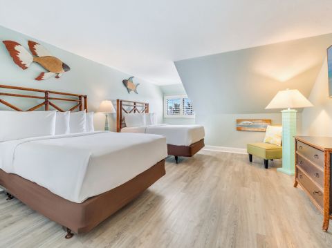 Spacious bedroom with two queen beds, coastal artwork, and light wood flooring