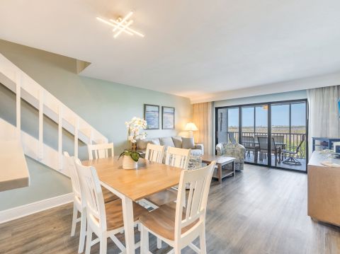 Dining space with a wooden table and white chairs next to a staircase and pastel green walls