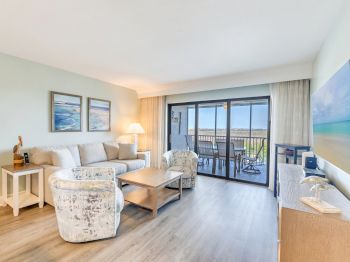 Living room with plush seating, wood floors, and a balcony view of the ocean.