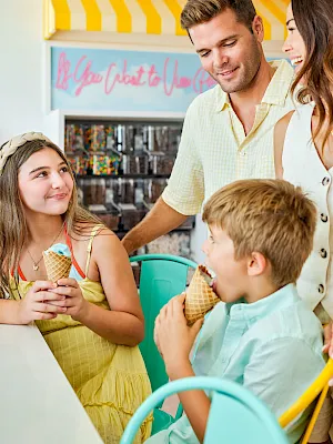 A family enjoys ice cream in a shop, with an attendant serving a child at the counter.