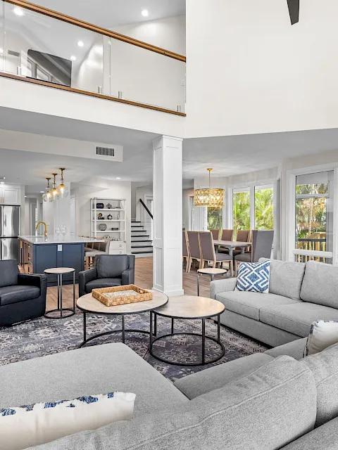 A modern open-plan living room with gray sofa, coffee table, and a bright kitchen with cabinets and stainless appliances.