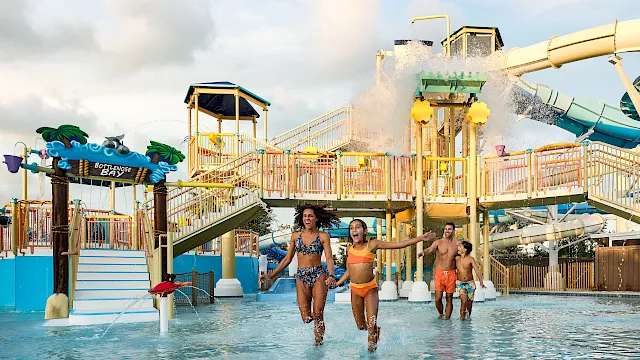 Kids at a water park splash in a pool as a slide shoots water high into the air.