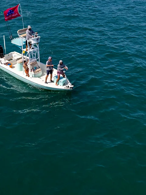 A small boat at sea with crew onboard hoisting a red flag, with open water stretching around them.