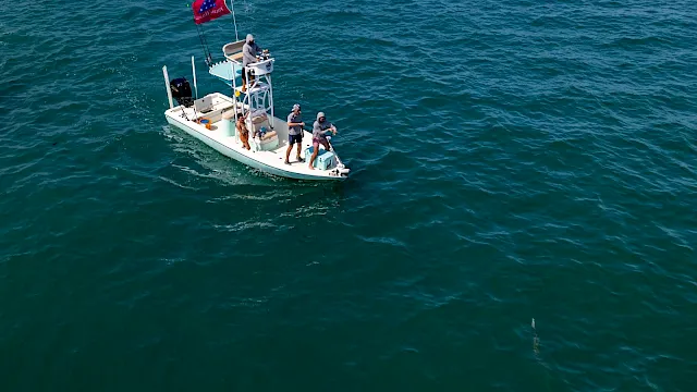 A small boat at sea with crew onboard hoisting a red flag, with open water stretching around them.