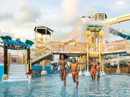 Kids splash in a water park as a huge tipping bucket dumps water from a slide into the pool.